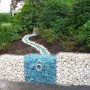 Gabiona Gabionenkorb als dekorative Gartenmauer mit Steinen und blauen Glassteinen.
