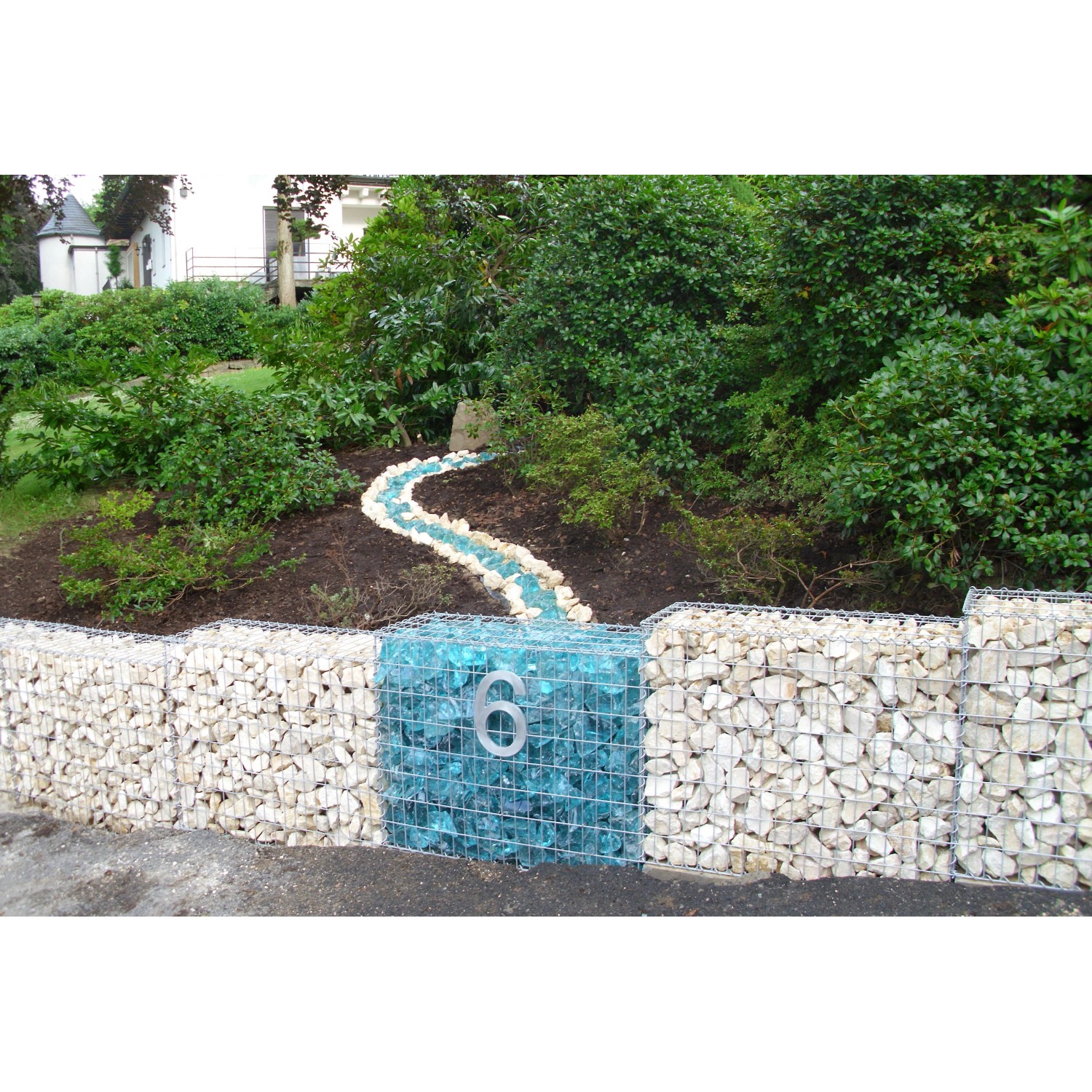 Gabiona Gabionenkorb als dekorative Gartenmauer mit Steinen und blauen Glassteinen.