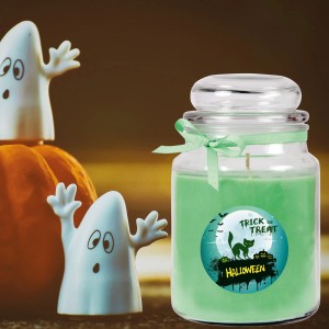 Grüne HS Candle Duftkerze im Glas mit Halloween-Motiv, neben Kürbis und Geistern.