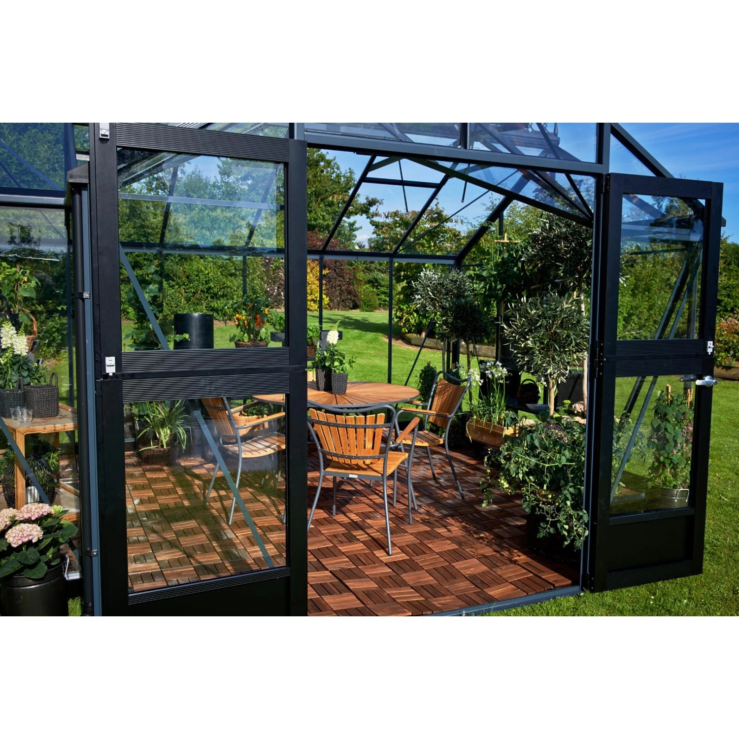 Juliana Gewächshaus Orangerie 15, schwarz-anthrazit, mit Sitzgruppe und Pflanzen.