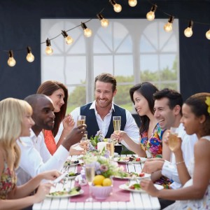 Szene mit Partyzelt: Gruppe feiert mit Sekt an gedecktem Tisch unter Lichterkette.