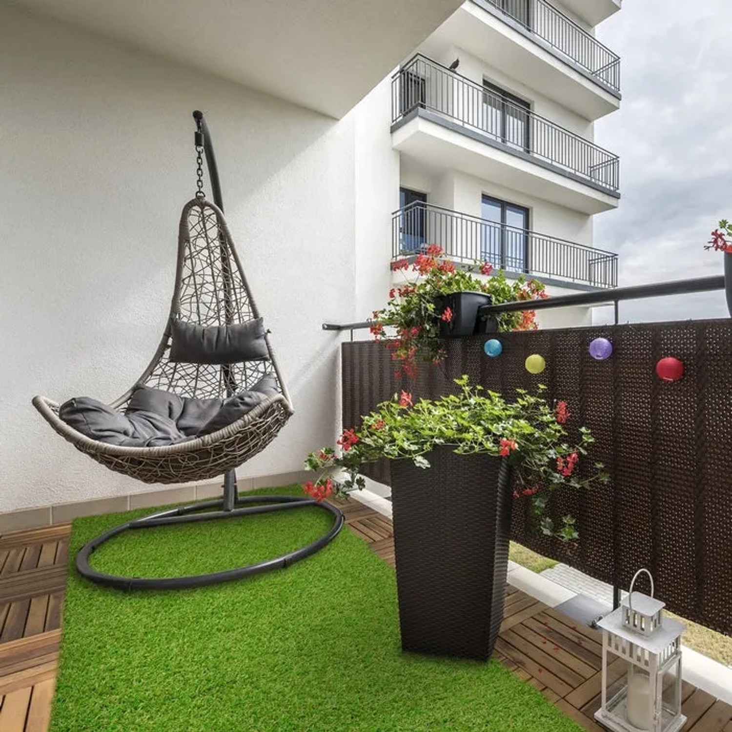 Grüner Karat Kunstrasen Riviera auf einem Balkon mit Hängesessel und Pflanzen.