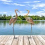 Zwei metallene Kranich Gartenstatuen auf einem Holzsteg am Seeufer. Eine Figur blickt nach unten, die andere nach oben.