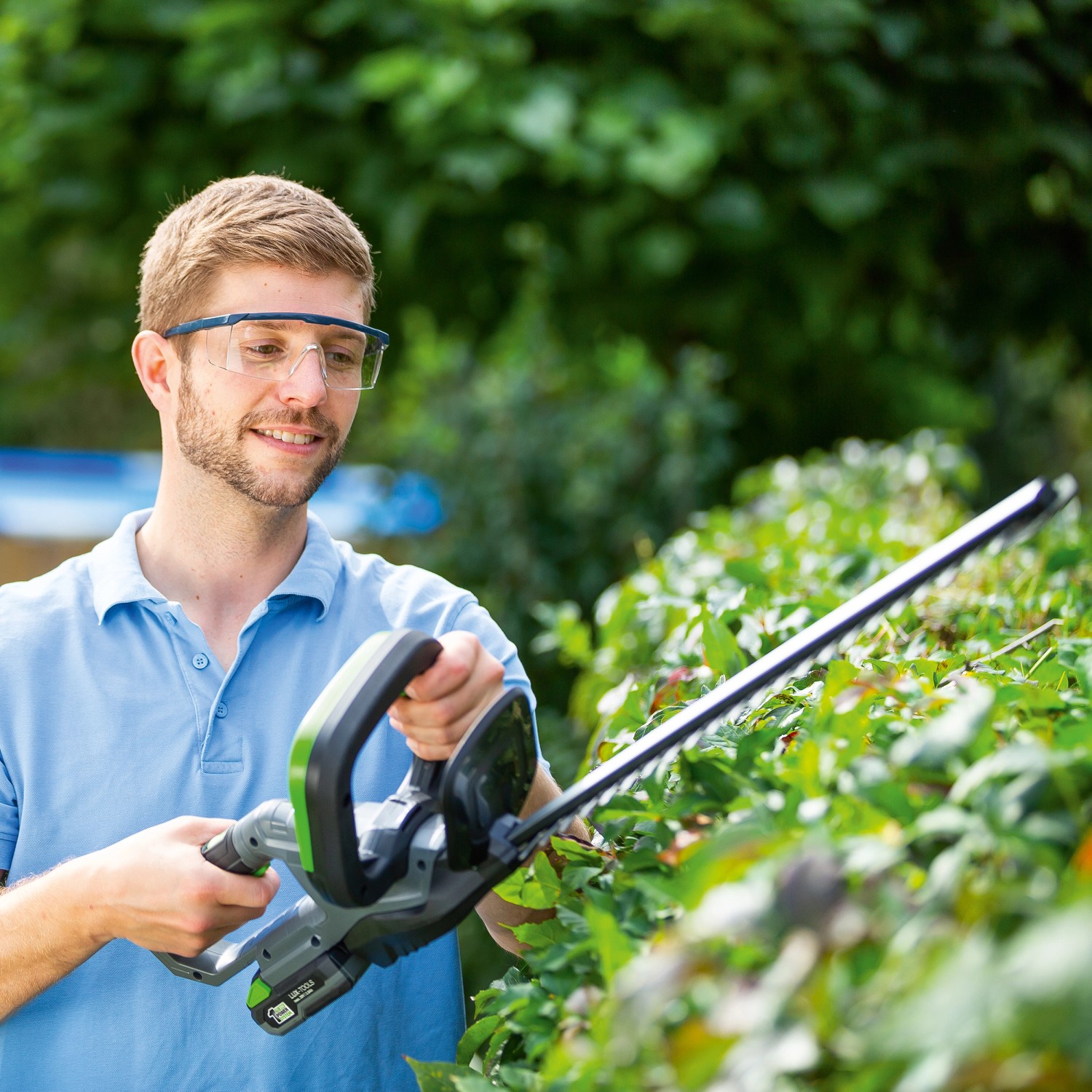 Mann schneidet Hecke mit LUX Akku-Heckenschere A-HS-20/52 aus dem 1 PowerSystem.