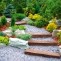Gartenweg mit Unkrautvlies unter Kies, Holzstufen und Pflanzen.