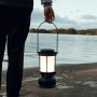 Schwarze Petromax LED-Laterne PX-LM500, gehalten von einer Person vor einem See. Camping Leuchte mit 160h Leuchtdauer.