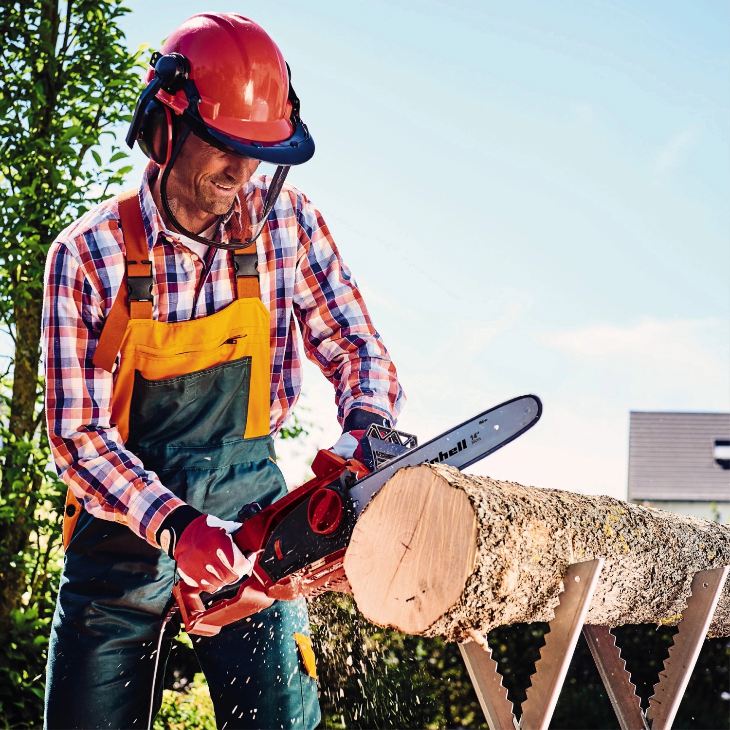 Mann sägt Holz mit der roten Einhell Elektro-Kettensäge GH-EC 1835 und Schutzkleidung.