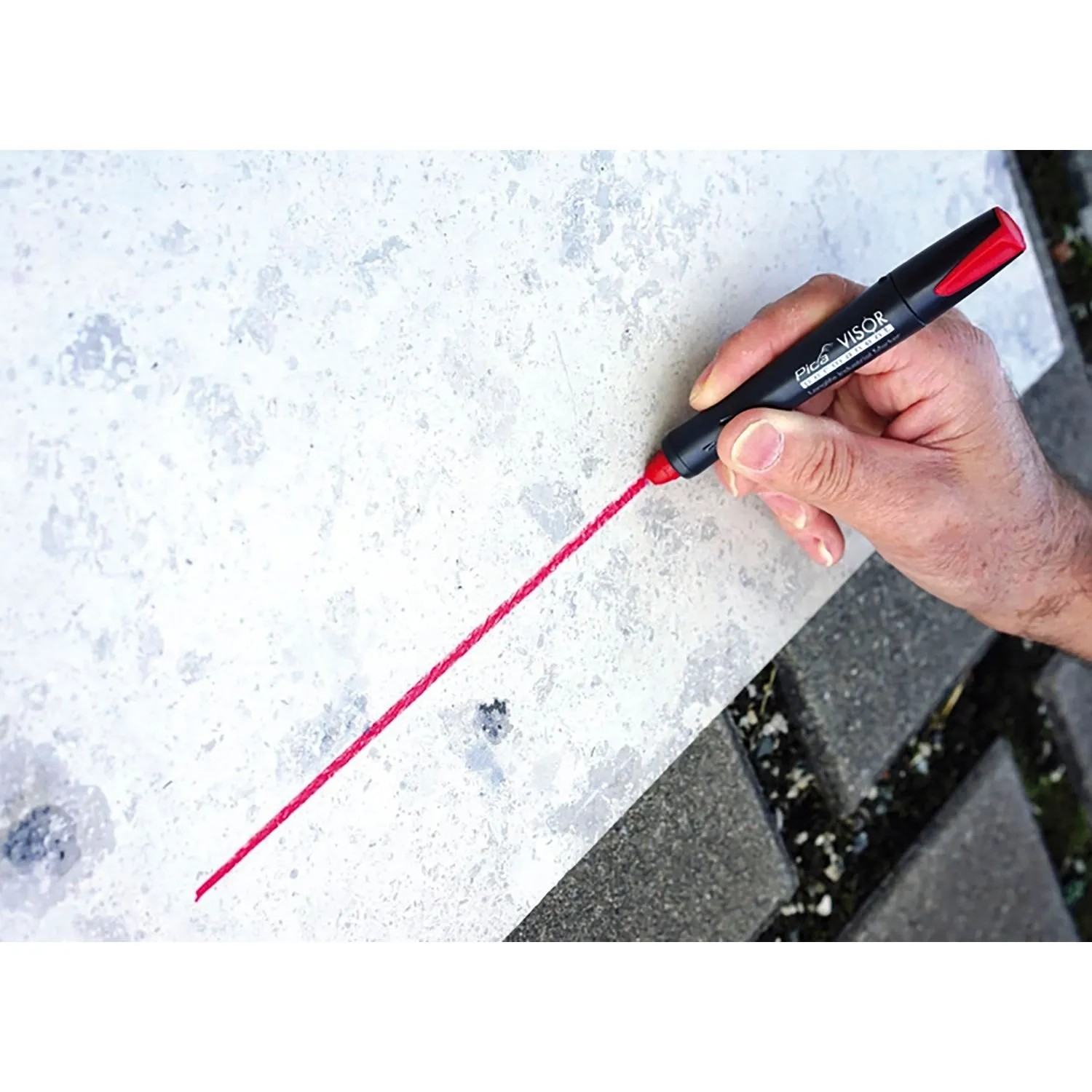 Hand markiert mit rotem Pica Visor 990 Permanentmarker eine präzise Linie auf Beton. Vielseitiges Handwerkzeug.