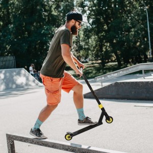 Mann fährt HOMCOM Stuntscooter (gold) auf Rampe im Skatepark. Aluminium-Metall-Roller.
