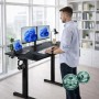 Mann steht an schwarzem, elektrisch höhenverstellbarem Schreibtisch mit Monitoren. Ergonomischer Steh-Sitztisch für Home Office.