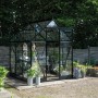 Schwarzes Halls Gewächshaus Icon 6 mit Glasfront und Pflanzen im Garten.