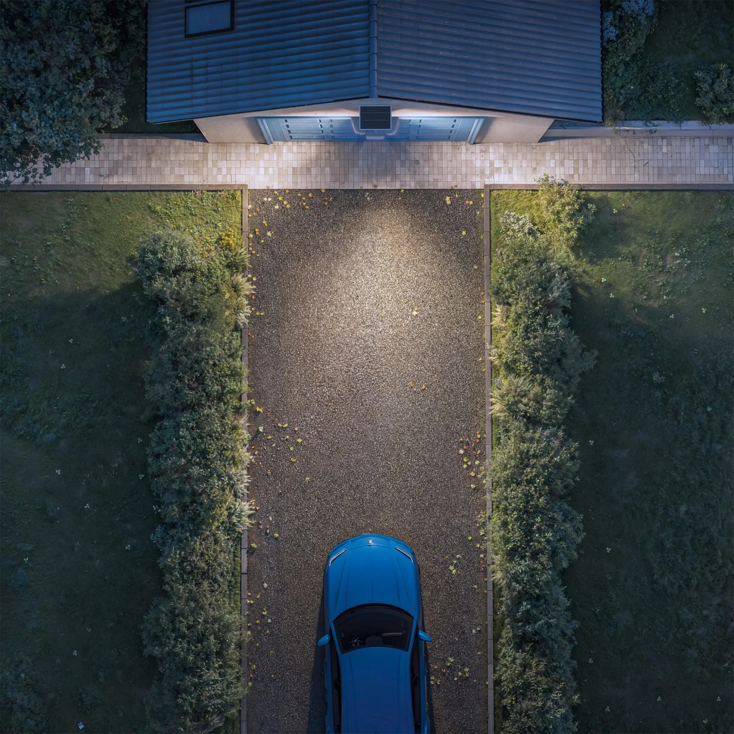 Philips Zyren Solar-LED-Außenstrahler beleuchtet Hofeinfahrt mit Auto, Vogelperspektive.