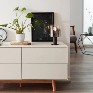 Brilliant Tischleuchte Beth Rauchglas auf Kommode im Wohnraum. Design-Tischlampe mit E27 Fassung.