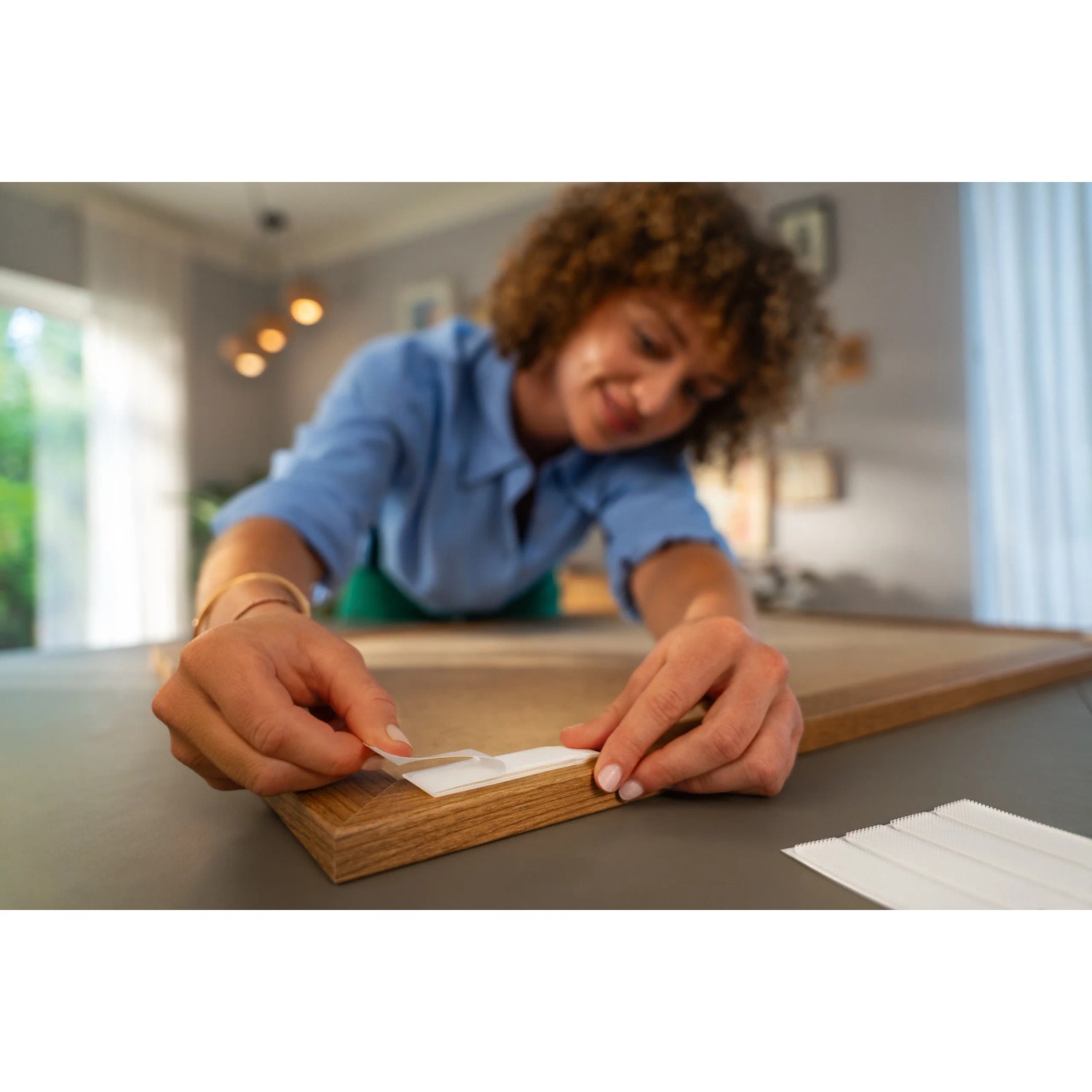 Frau befestigt Bilderrahmen mit Tesa Powerstrips Click-Small Klebenägeln an der Wand.