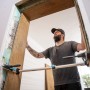 Mann montiert Türzarge mit wolfcraft Türfutter-Montageset Pro. Silberne Spannwerkzeuge fixieren den Holzrahmen präzise.