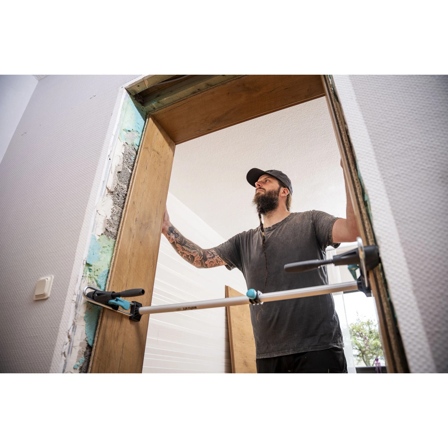 Mann montiert Türzarge mit wolfcraft Türfutter-Montageset Pro. Silberne Spannwerkzeuge fixieren den Holzrahmen präzise.