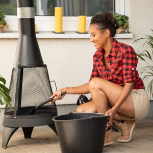 Frau reinigt Outdoor-Kamin mit schwarzer Relaxdays Kohlenschaufel aus Stahl. Flache Ascheschaufel für Grillzubehör.