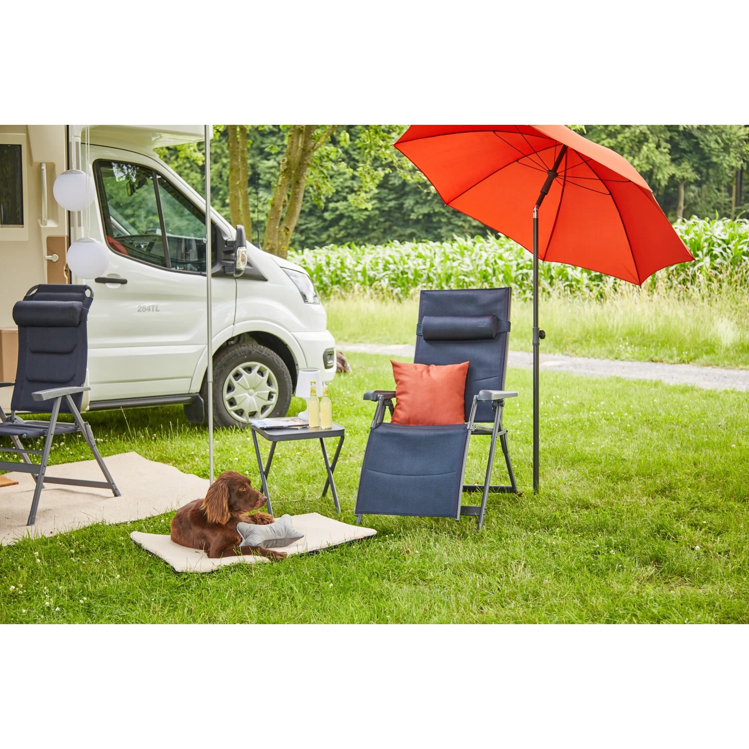 Dunkelblaue Siena Garden Campingrelaxliege Premium XL mit rotem Sonnenschirm und Hund im Garten.