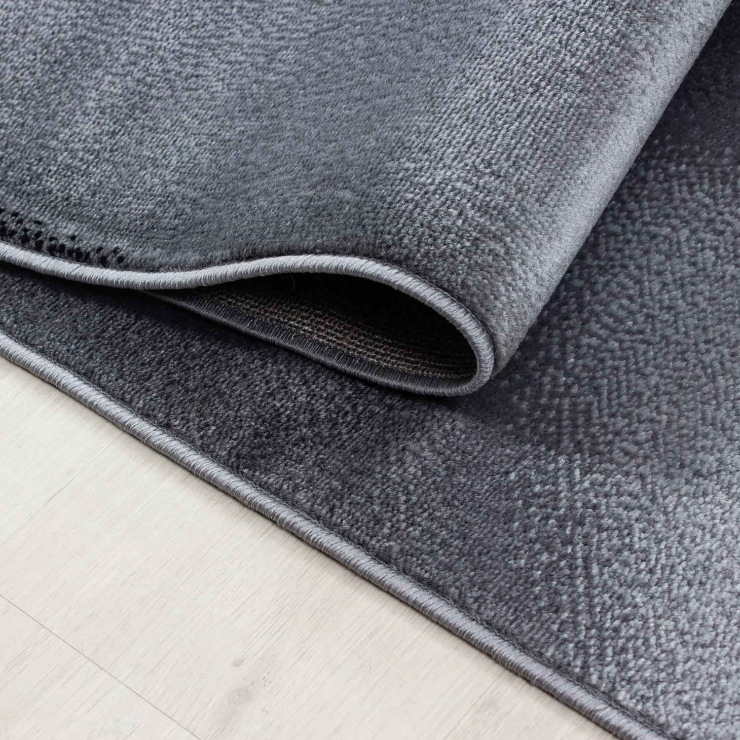 Ayyildiz Kurzflorteppich Plus, schwarz, 80x150 cm, Detailansicht der Textur und des umgeschlagenen Teppichs.