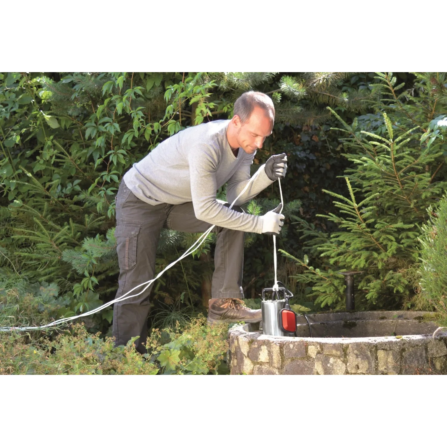 Mann bedient Einhell Schmutzwasserpumpe GC-DP 1020 N am Brunnen. Fördermenge 18.000 l/h.