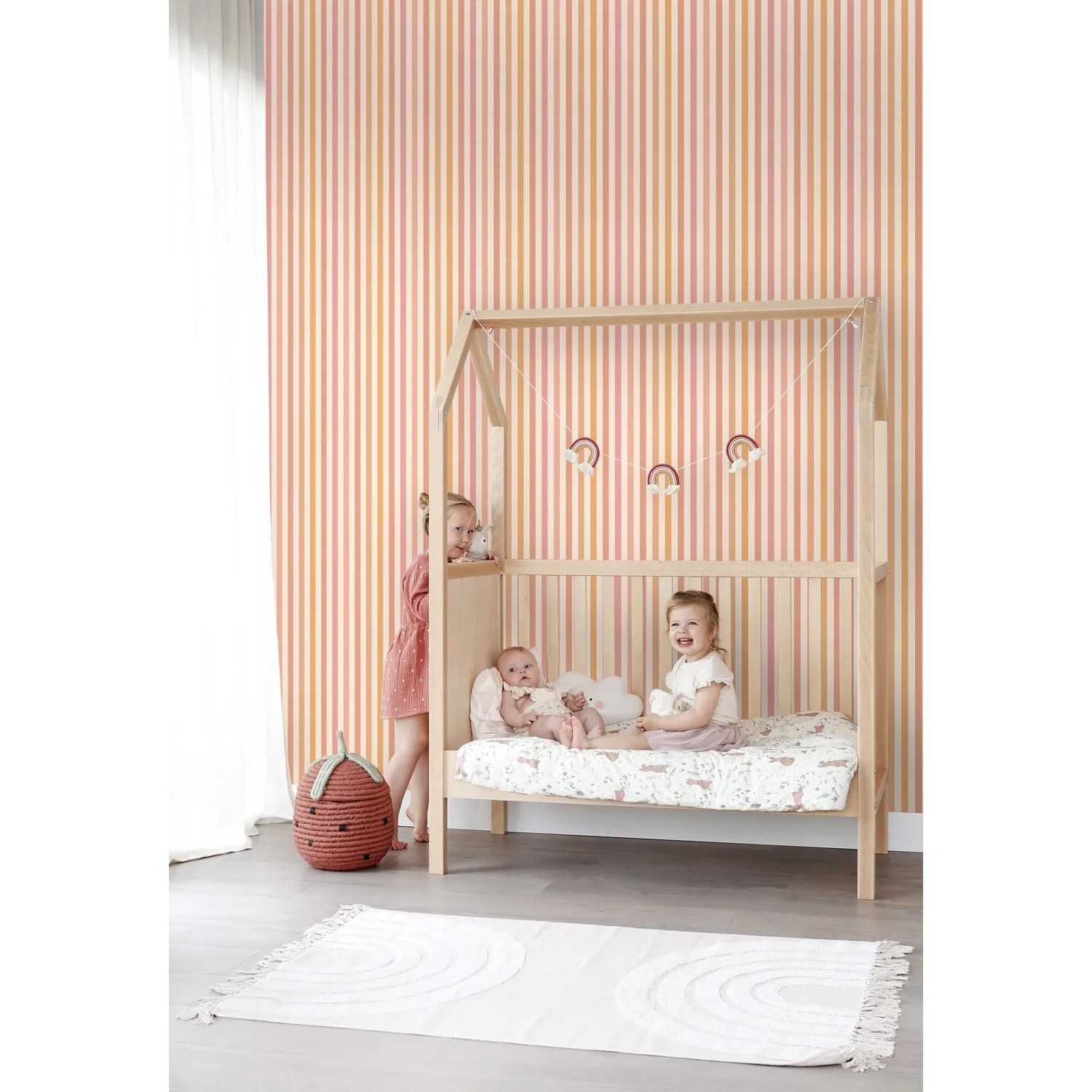 Kinderzimmer mit ESTAhome Streifen Tapete in Orange und Rosa, Bett und spielenden Kindern.