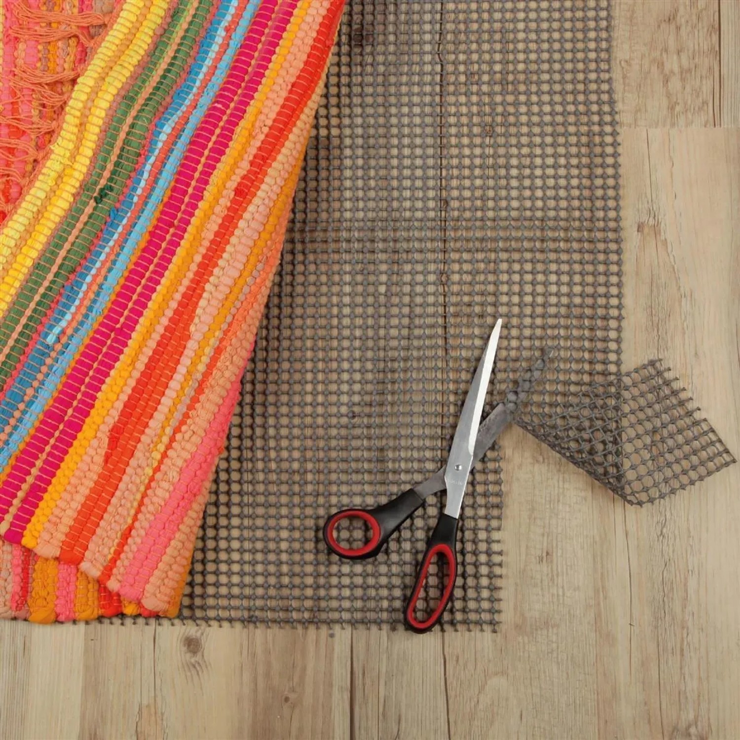 Dunkelgrauer ProHome Teppich Gleitschutz (80x150 cm) mit Schere auf Holzboden.
