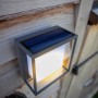 Moderne Lutec LED Solar-Wandleuchte Curtis mit Bewegungsmelder und Solarpanel an einer Holzwand.