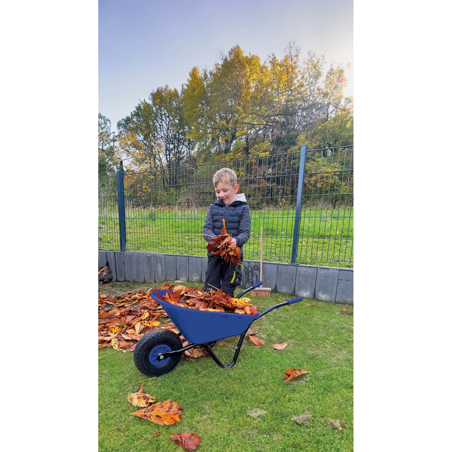 Pro-Bau-Tec Kinderschubkarre (Blau, 20 l) mit Kind beim Laub sammeln im Garten.
