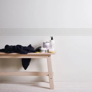 Weiße, selbstklebende Bordüre mit Mäandermuster im Bad über einem Holzbänkchen.