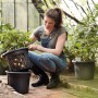 Schwarzer Elho Kartoffeltopf Green Basics Living (Ø 32,3 cm) mit Frau beim Bepflanzen im Gewächshaus.