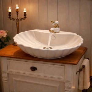 Ovales Aufsatz-Waschbecken in Muschel-Form aus glänzender Keramik mit goldener Armatur im eleganten Badezimmer.