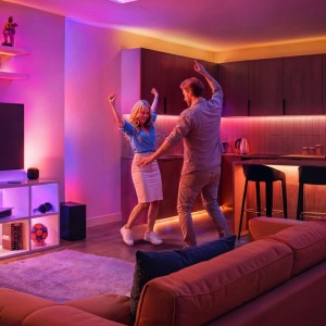Paar tanzt in modernem Wohnzimmer mit farbiger Philips Smart-LED-Beleuchtung. Wallwashing-Effekt, Millionen Farben, Ambiente.