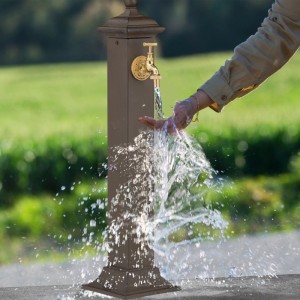 Dunkelbrauner Relaxdays Standbrunnen aus Gusseisen mit goldenem Hahn, Wasser läuft.