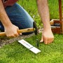 Gardena Begrenzungskabel Installation: Mann befestigt Draht für Mähroboter mit Hammer im Garten.