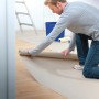 Mann rollt LUX Auslegepapier (1 m x 100 m) zum Abdecken auf einem Holzboden aus.