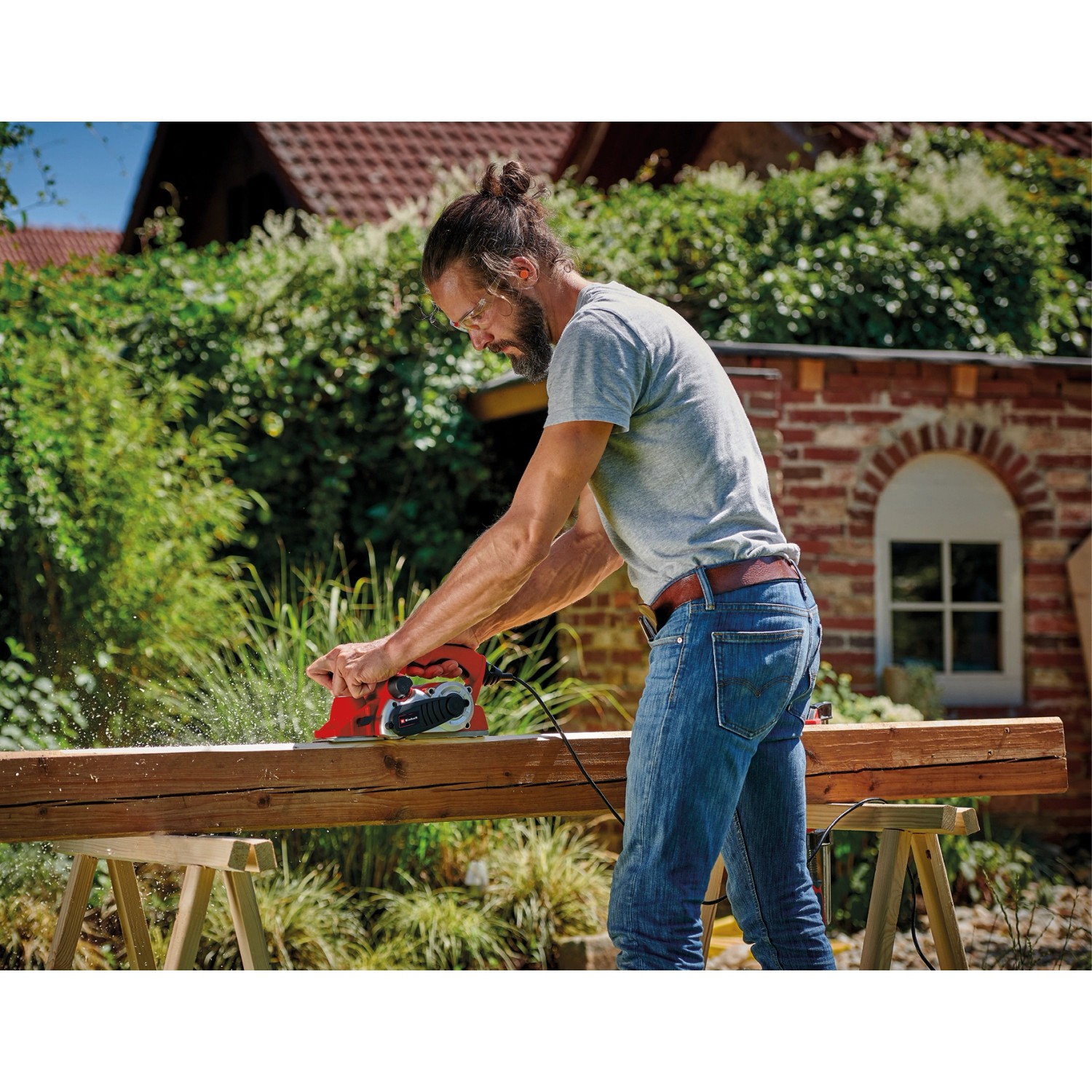 Mann hobelt Holz mit dem roten Einhell Elektrohobel TE-PL 900 im Garten.