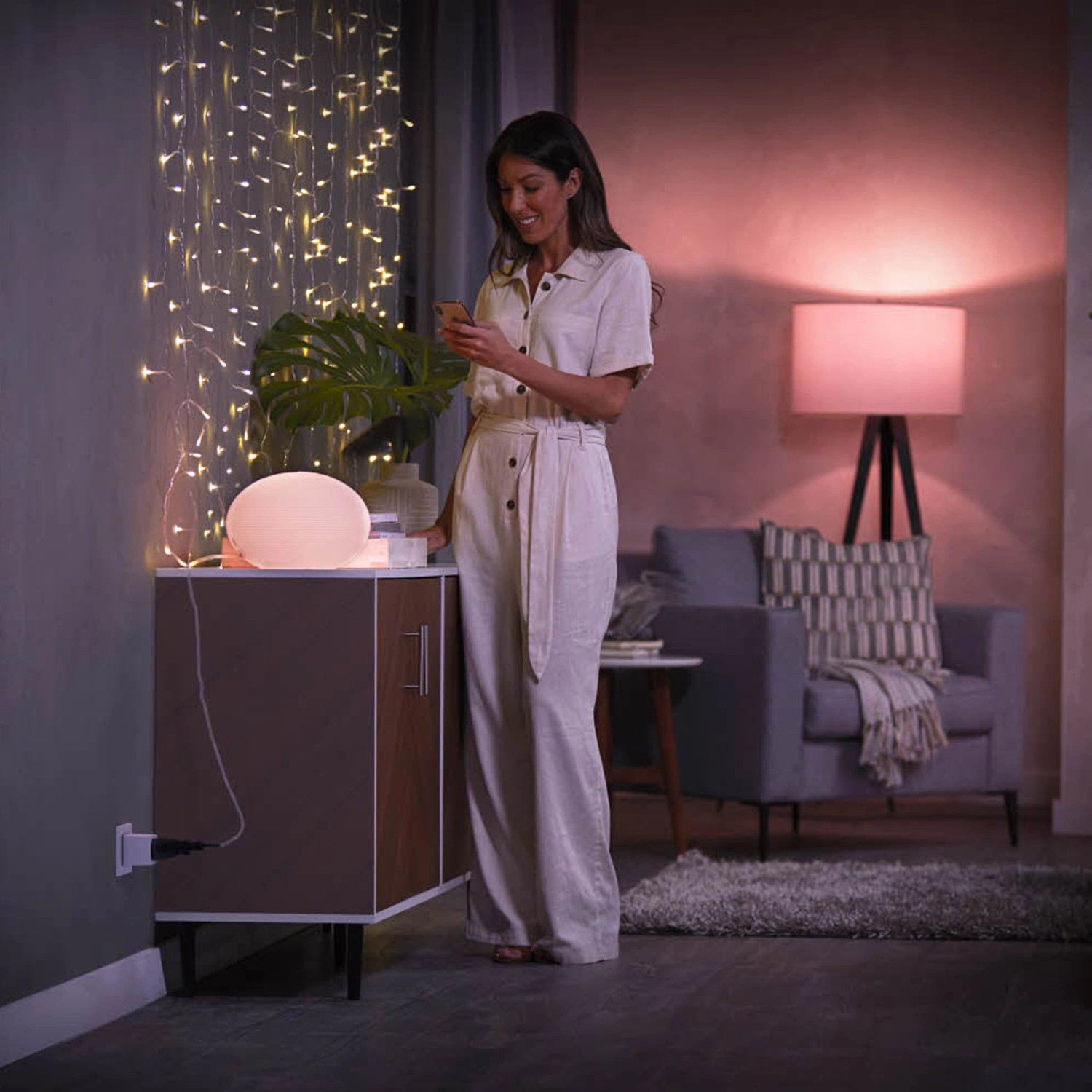 Philips Hue Smart Plug Steckdose in Weiß im Wohnraum mit Lampe und Frau mit Smartphone.