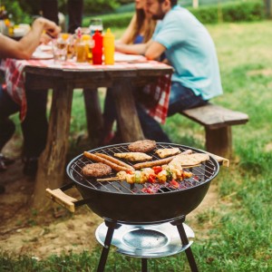 Grillszene mit Grillgut und Personen im Hintergrund. Grillzubehör wie Kohlekörbe sind nicht sichtbar.