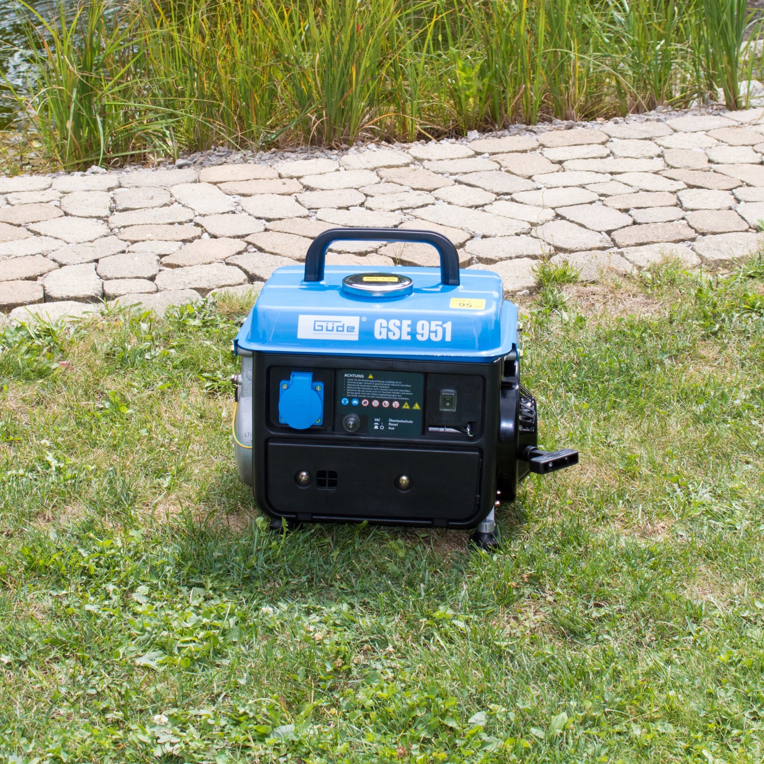 Blauer Güde Stromerzeuger GSE 951 auf Rasen. Kompakter 2-Takt-Benzingenerator mit Tragegriff.
