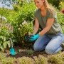Frau pflanzt mit Gardena Gartengeräte-Set Blumenkelle, Unkrautstecher und Handschuhen im Garten.