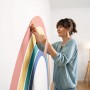 Frau klebt mit Tesa Malerband Kurven einen Regenbogen an die Wand.