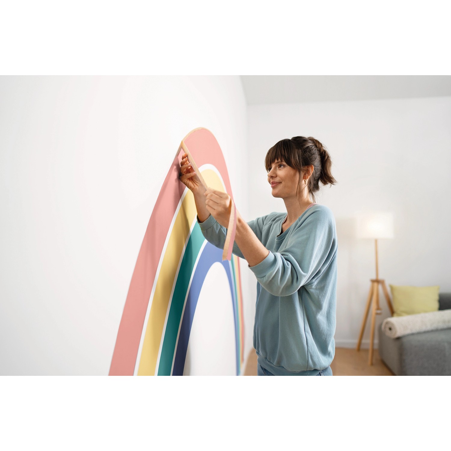 Frau klebt mit Tesa Malerband Kurven einen Regenbogen an die Wand.