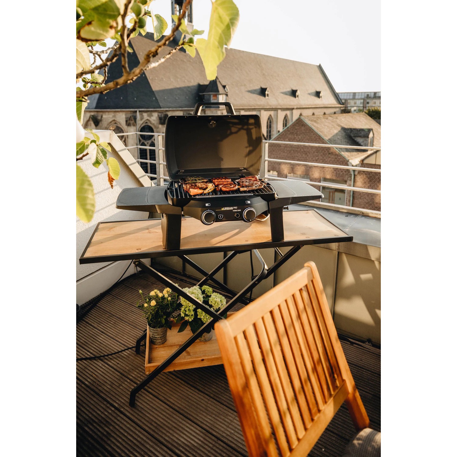 Enders Elektrogrill eUrban Pro 2 Turbo Mobil auf Tisch mit Grillgut, im Hintergrund Gebäude.
