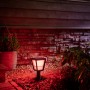 Philips Hue Econic LED Sockelleuchte im Garten mit rotem Licht. Wetterfeste Außenleuchte für stimmungsvolle Beleuchtung.