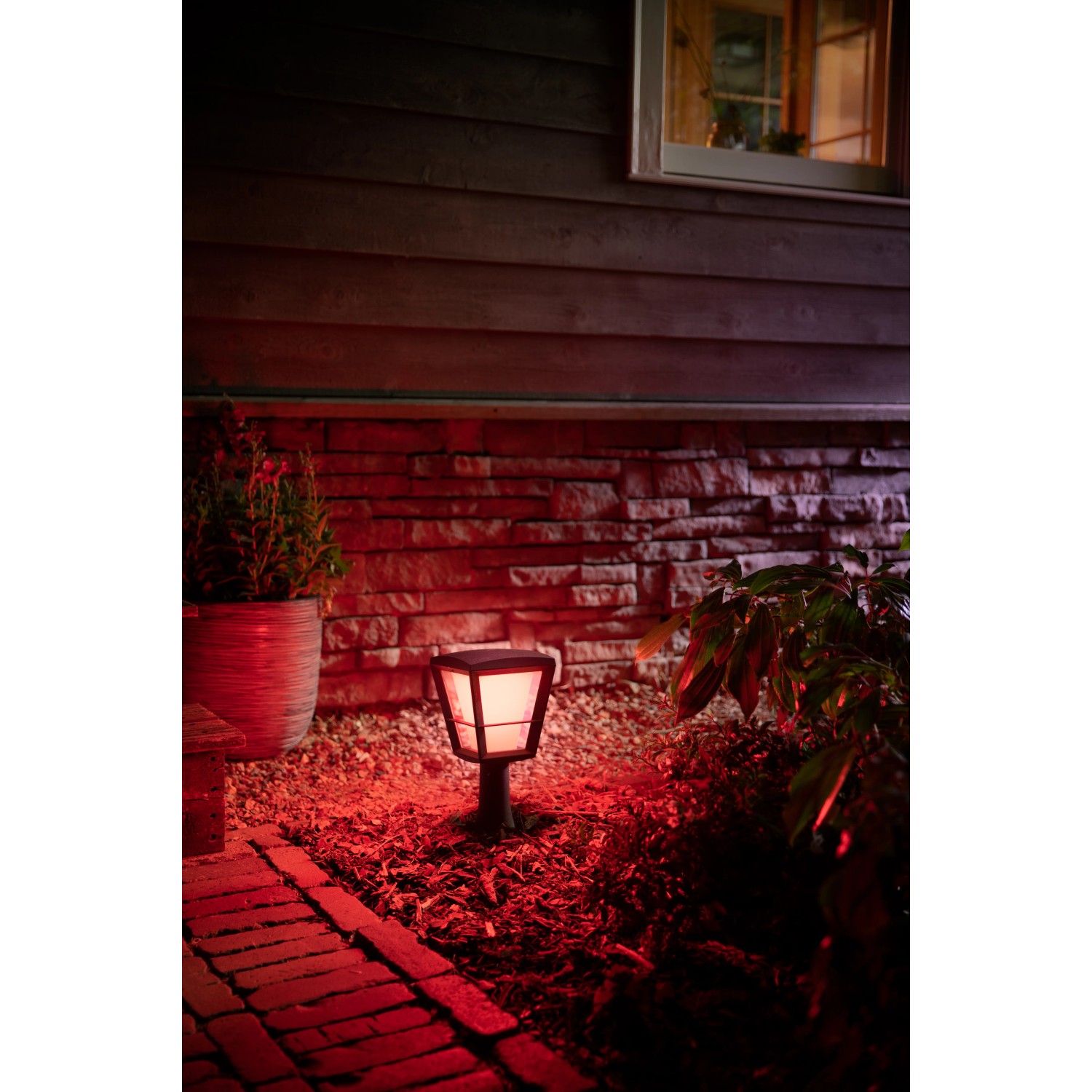 Philips Hue Econic LED Sockelleuchte im Garten mit rotem Licht. Wetterfeste Außenleuchte für stimmungsvolle Beleuchtung.