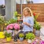Frau schneidet Schlauch des Gardena Solar-Bewässerung Aqua Bloom Sets auf Terrasse mit Pflanzen.