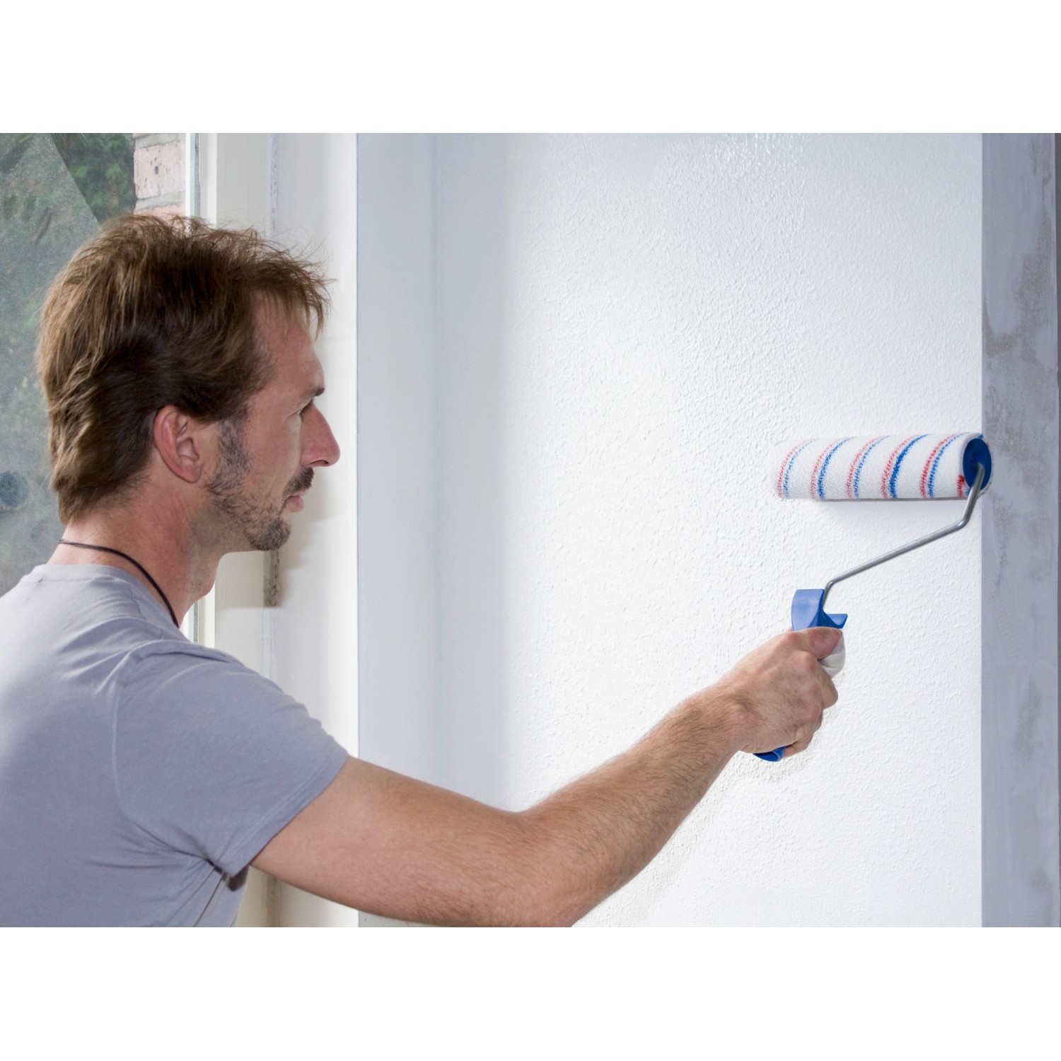 Mann trägt Knauf Easy Putz Fein mit Farbroller auf Wand auf. Putz mit 1 mm Körnung.