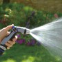 Hand hält regulierbare Gartenspritze, Wasserstrahl im Garten.