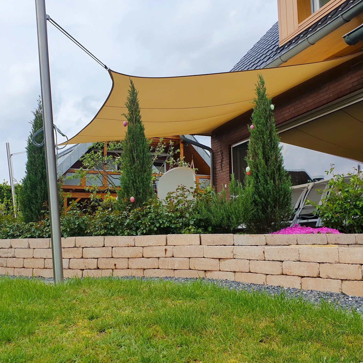 Sandfarbenes Toldoro Sonnensegel Komplettset mit Edelstahl-Halterung im Garten.