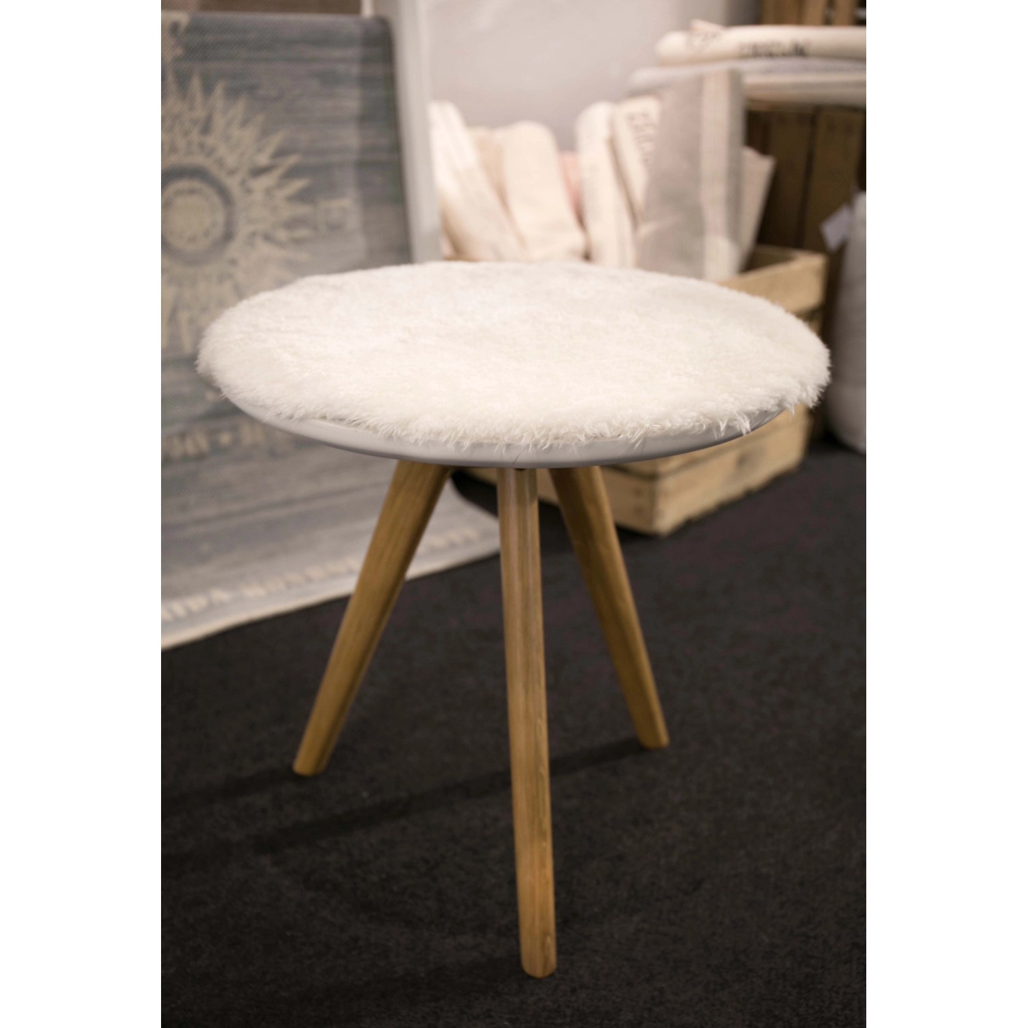 Weißes, rundes Sitzkissen Lambskin aus Kunstfell, 40x40 cm, auf einem Hocker mit Holzbeinen.